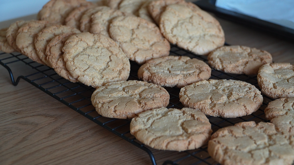 Golden ginger nut biscuits cooling on a black wire rack after baking
