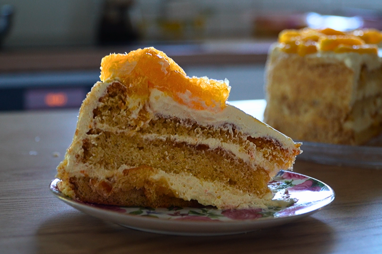 A slice of flourless almond cake layered with marmalade and cream, topped with fresh orange, served on a floral plate.
