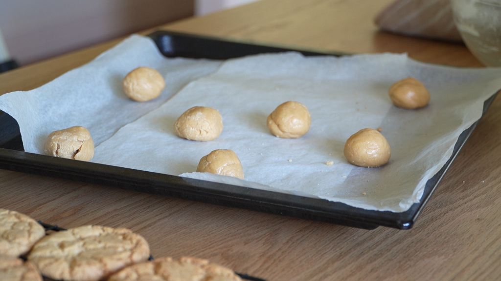 Unbaked ginger nut biscuit dough rolled into balls on a tray lined with baking paper
