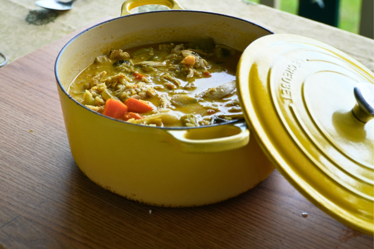 Golden curry chicken soup in a bowl, filled with vegetables, rice, and shredded chicken.