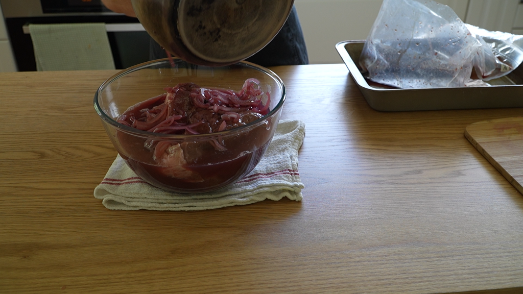 Pouring marinade with onions over topside beef in a glass bowl