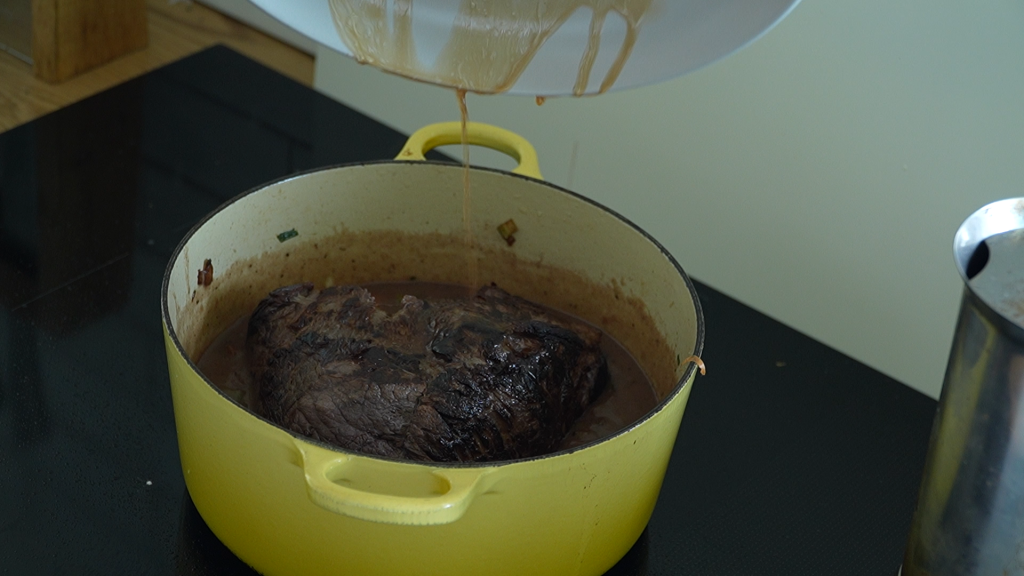 Browned topside beef being placed back in the pot with sauce before oven braising.