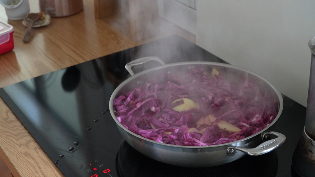 A steaming skillet of red cabbage and apple slices cooking together on the stovetop