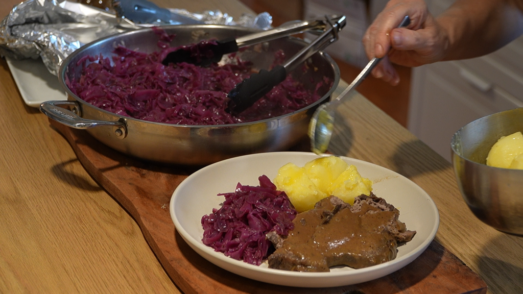 Hand plating Sauerbraten with red cabbage and boiled potatoes, served with rich sauce.