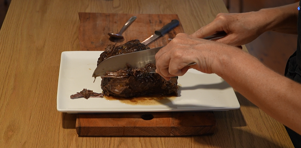 Close-up of hands slicing tender sauerbraten beef on a white plate