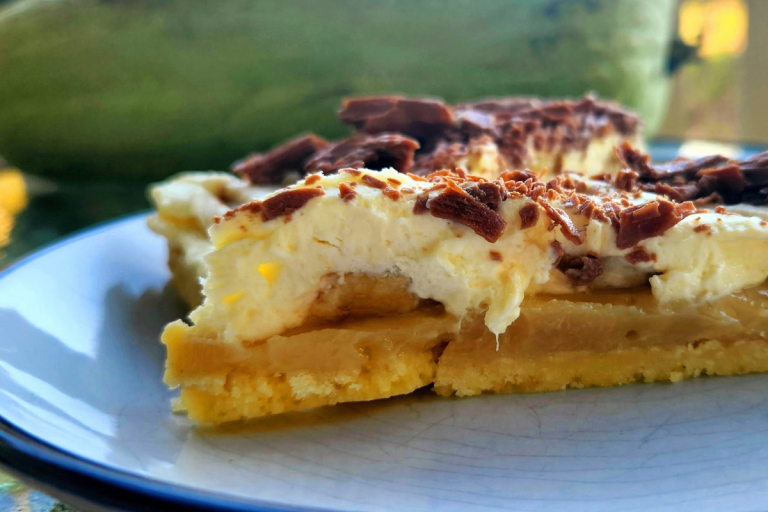 Closeup of a slice of Banoffee Pie showing cream, bananas, caramel, and chocolate shavings