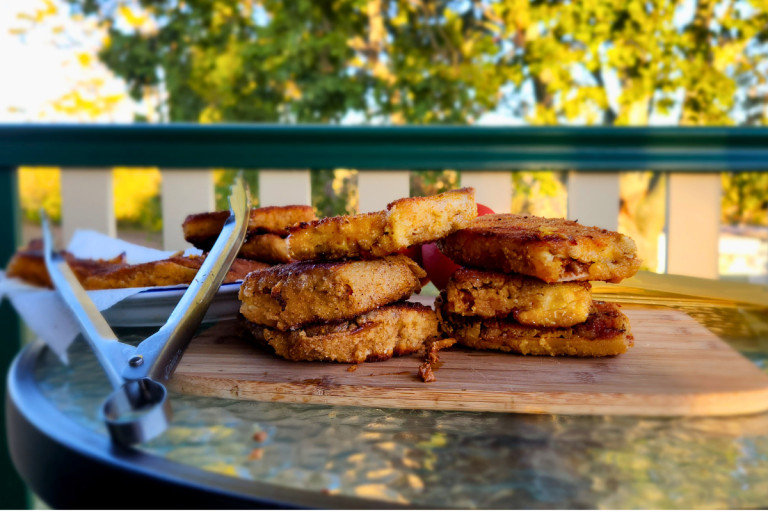 Golden fried lasagna toppers stacked on a wooden board outdoors