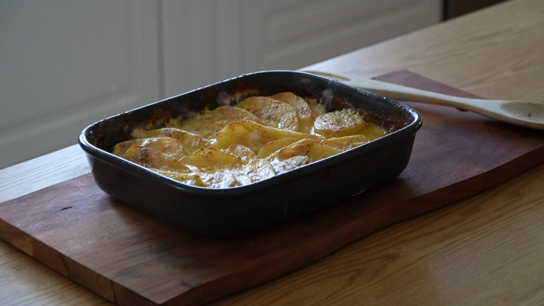 A serving spoon lifting buttery scalloped potatoes from a baking dish