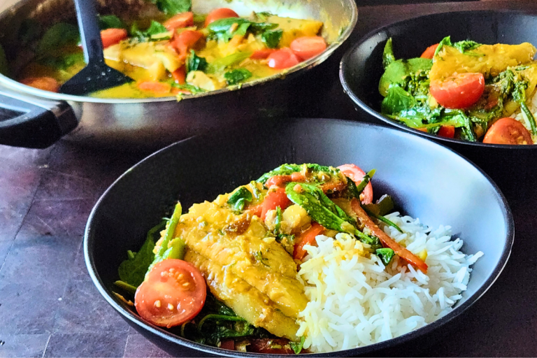 A black bowl of simple fish curry served over rice with cherry tomatoes, spinach, and capsicum.
