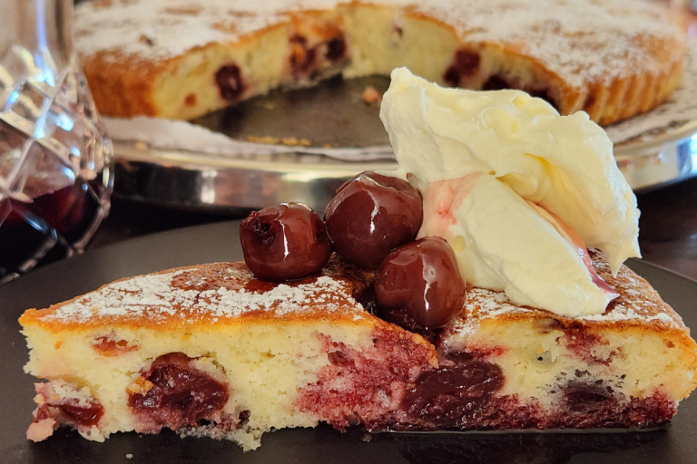 Close-up of a slice of cherry cake topped with whole cherries and whipped cream