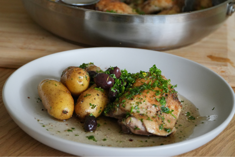 Plate of roasted chicken with fingerling potatoes and kalamata olives, with skillet in background