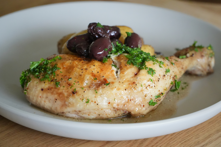 Close-up of roasted chicken leg with fingerling potatoes and olives, garnished with parsley
