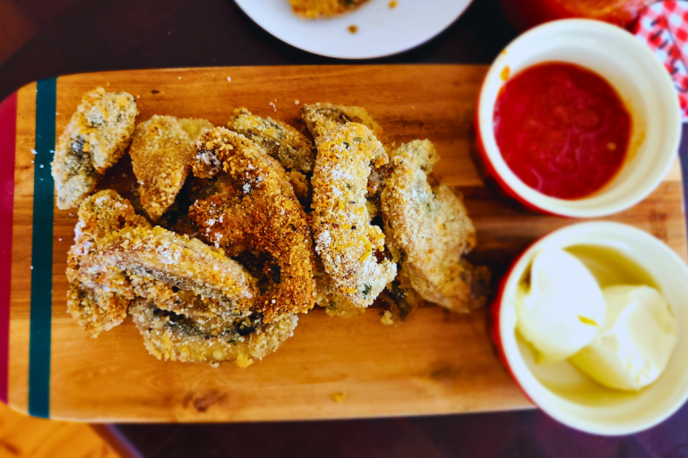 Crumbed mushrooms served on a wooden board with chili jam and sour cream