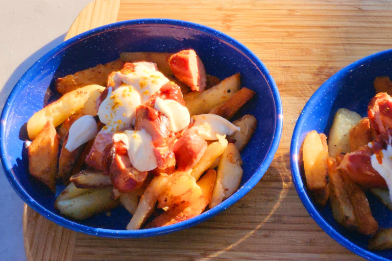 Bowl of currywurst with golden chips, mayonnaise, and curry ketchup on a wooden board
