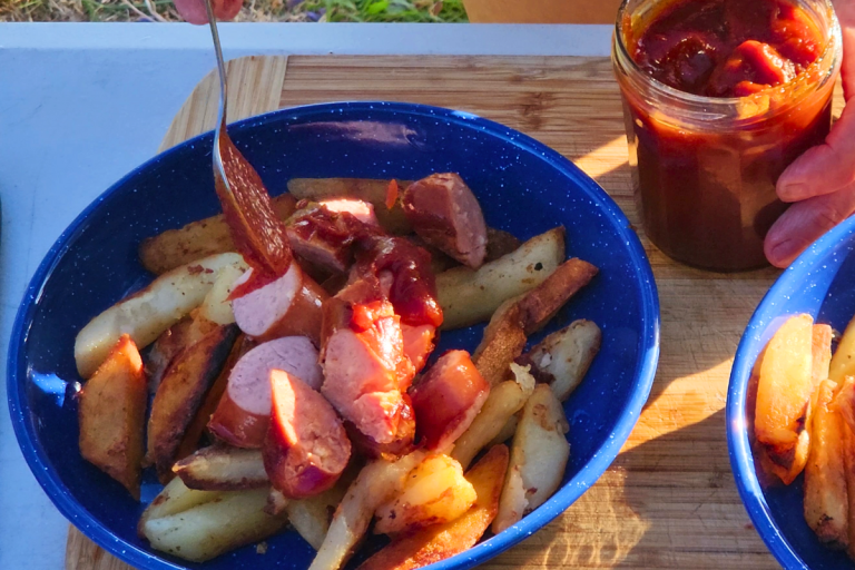 Sliced sausages and chips in a blue bowl with curry ketchup being spooned on top