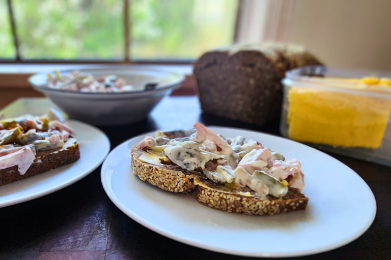 Fleischsalat served on buttered whole grain bread, with a bowl of salad and loaf in the background