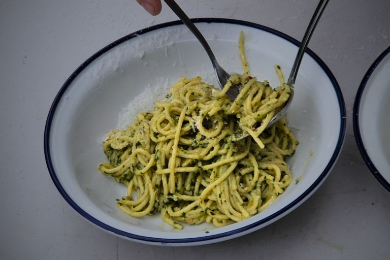Spaghetti tossed with pesto alla Genovese in a white enamel bowl