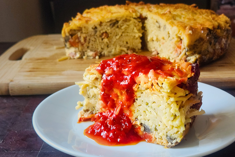 Slice of savoury spaghetti cake topped with tomato sauce, served on a white plate