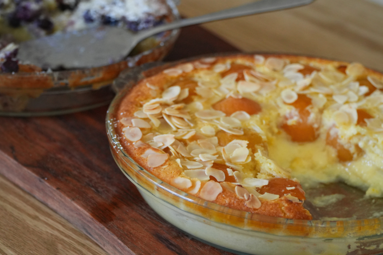 A close-up of an apricot and almond impossible pie with golden edges and flaked almonds on top.