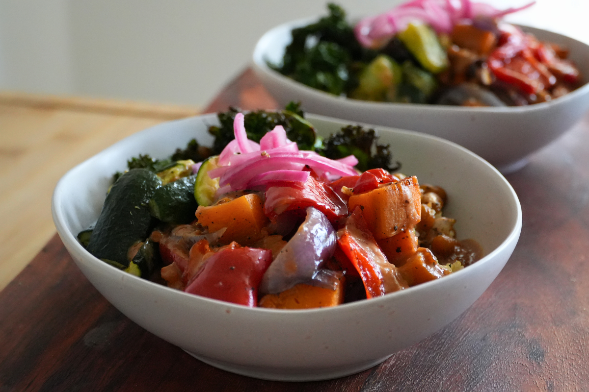 Two nourish bowls with roasted vegetables, chickpeas, kale, pickled onions and satay dressing.