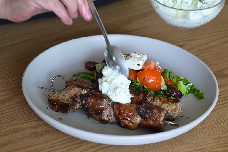 Close-up of Greek souvlaki with salad as tzatziki is spooned onto the meat.