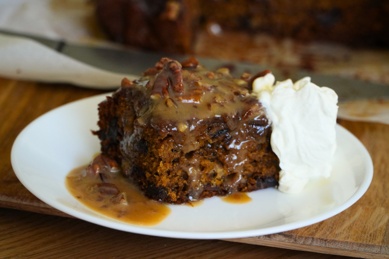 Sticky date pudding slice with glossy toffee sauce drizzle and whipped cream.