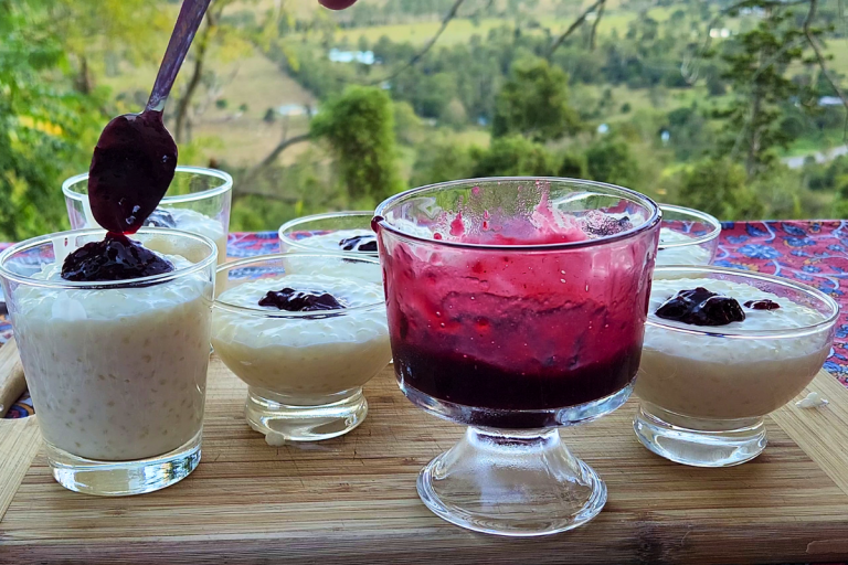 Creamy tapioca pudding in glass bowls topped with homemade berry jam, with a spoon drizzling jam into one.