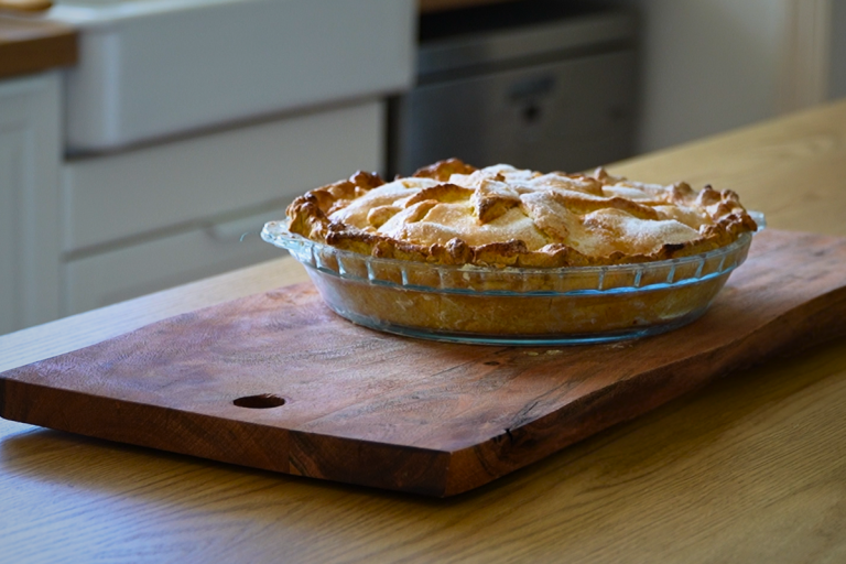 Homemade Australian apple pie with golden flaky pastry and spiced apple filling, cooling on a wooden board.