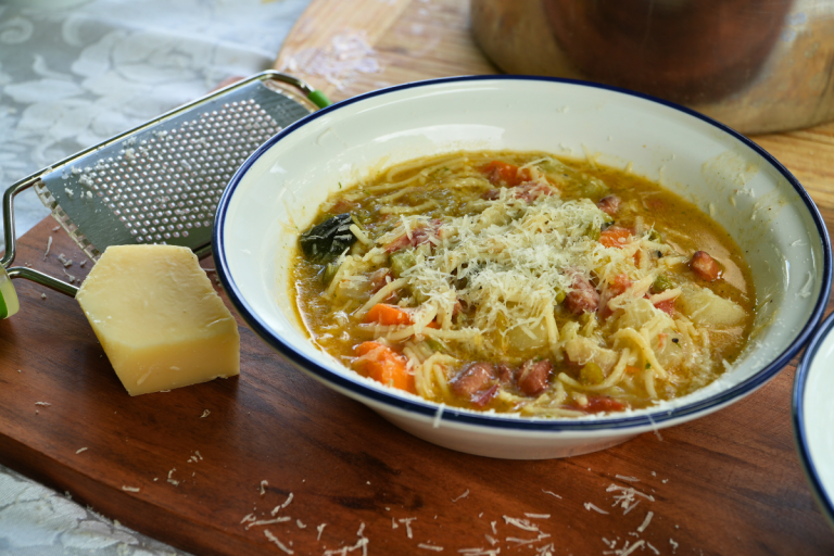 Hearty vegetable soup topped with grated cheese and basil pistou – a rustic bowl full of big flavour.
