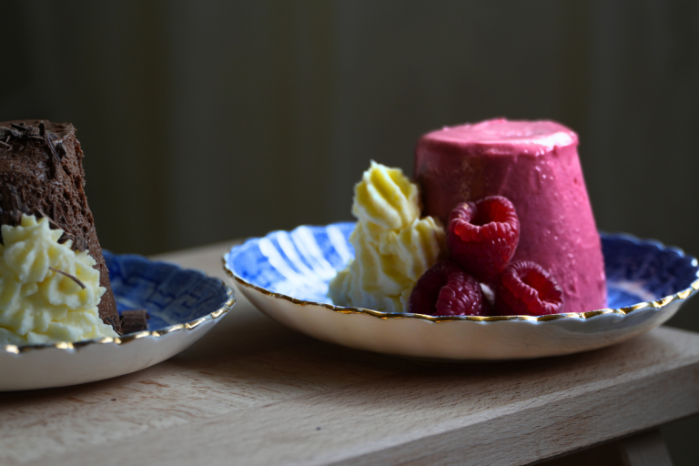 Raspberry mousse with fresh raspberries and whipped cream served in a blue and gold-rimmed dish.
