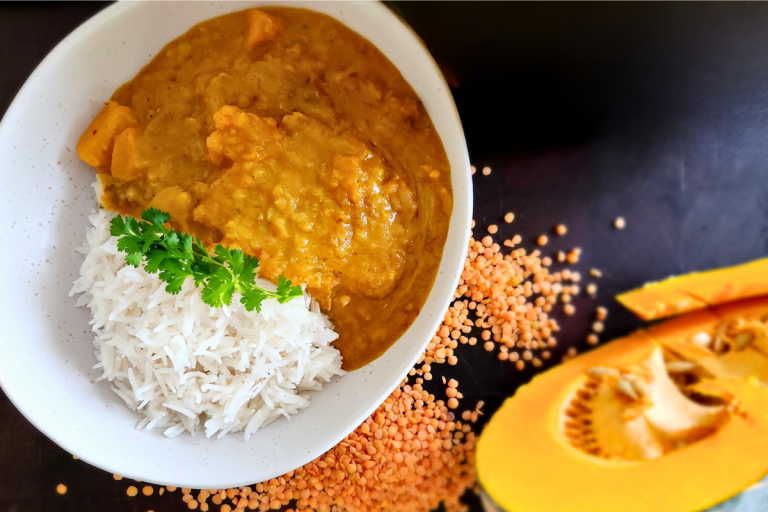 Bowl of pumpkin red lentil dal served with basmati rice, garnished with fresh coriander.