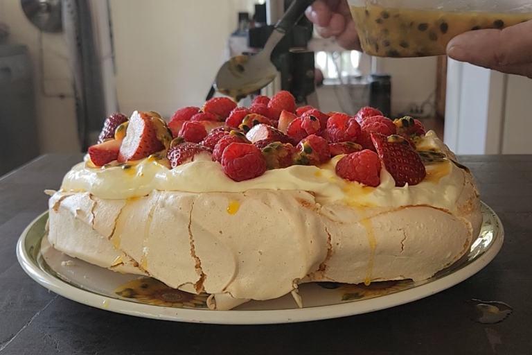 Easy Australian pavlova topped with whipped cream, strawberries, raspberries and passionfruit