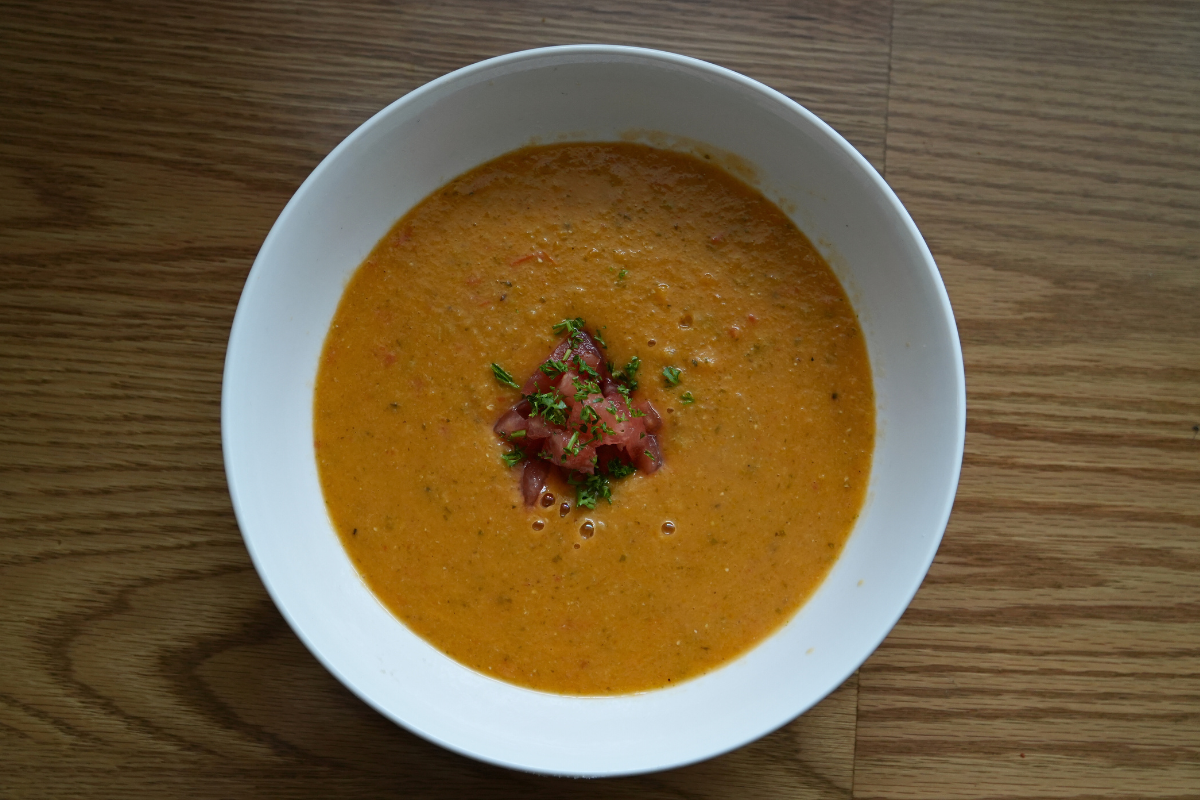 A bowl of red lentil, fresh tomato and basil soup garnished with chopped tomato and herbs on a wooden table.