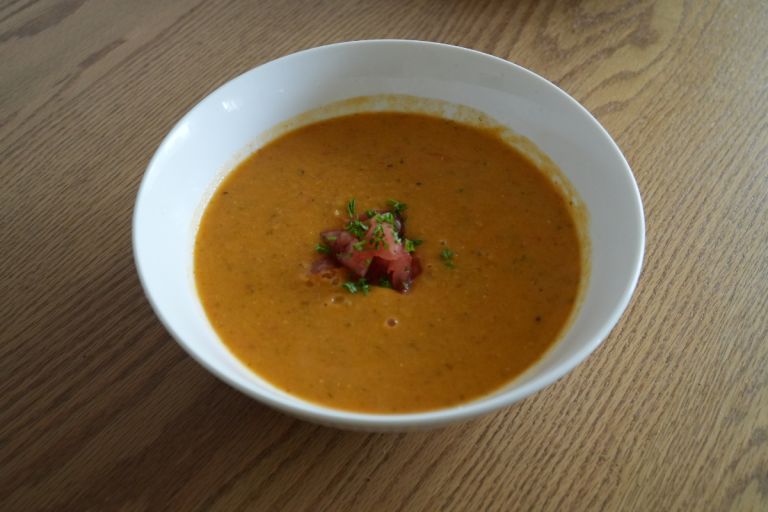 Side view of a bowl of red lentil, tomato and basil soup showing its creamy texture.
