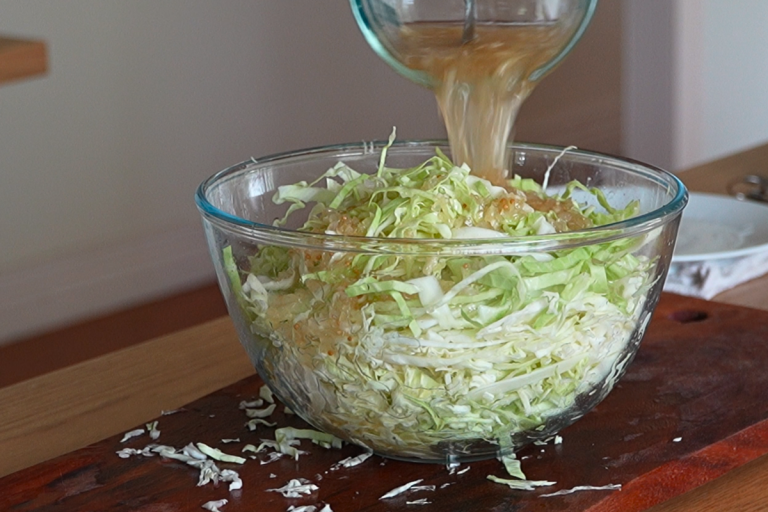 German dressing being poured over shredded cabbage in a glass bowl for homemade cabbage salad.