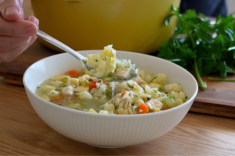 Spoon lifting homemade chicken soup with clear broth, vegetables, noodles and savoury custard