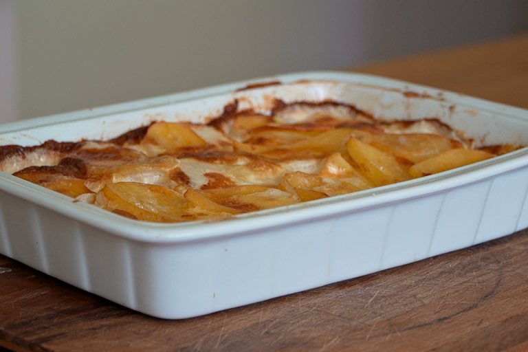 Golden creamy potato bake in white baking dish served as side dish for crumbed chops
