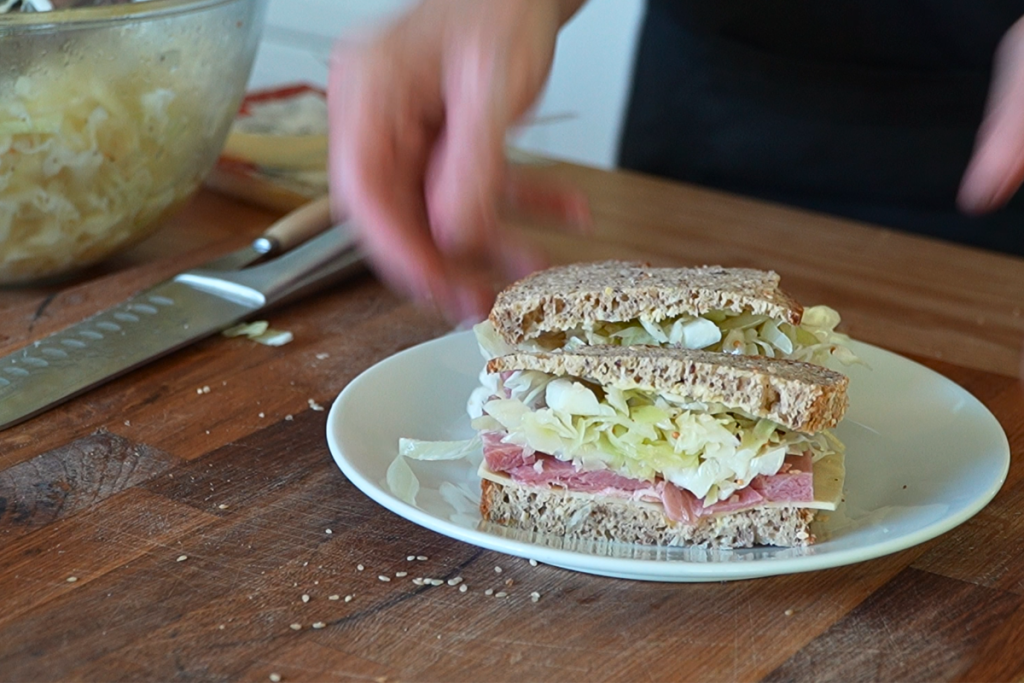Ham and cheese sandwich filled with homemade cabbage salad on a white plate.