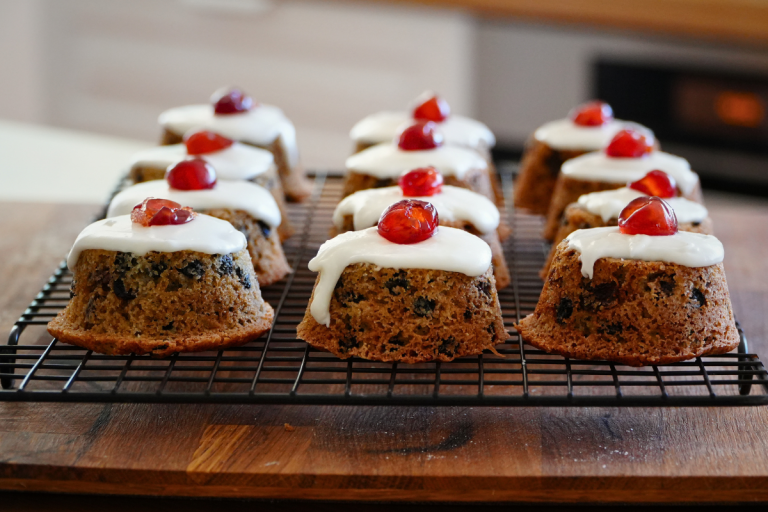 Little fruit cakes on a cooling rack topped with almond icing and glace cherries