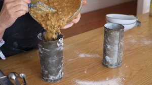 Date and walnut loaf batter being spooned into traditional old-fashioned roll tins