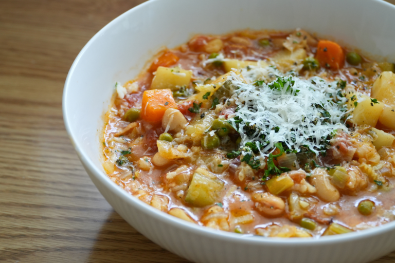Close-up of homemade minestrone soup with vegetables, beans, rice and parmesan cheese in a white bowl