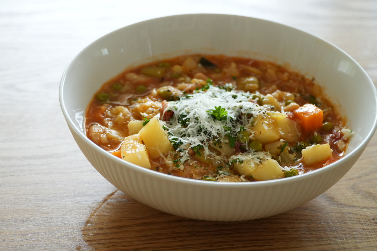 Healthy homemade minestrone soup topped with parmesan and herb garnish in a white bowl