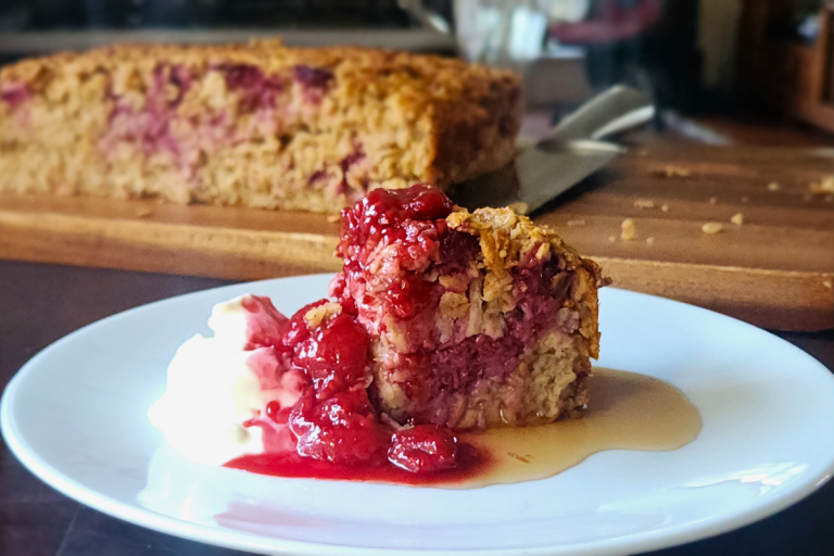 Slice of easy baked oatmeal with berries, berry coulis and yoghurt, with the baked oatmeal in the background